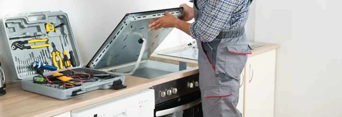 Cooktop repair technician lifting a built-in stovetop for service in Hollywood, FL