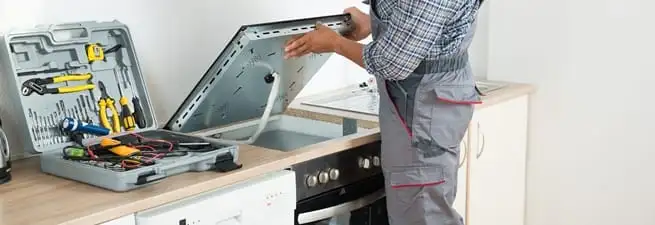 Cooktop repair technician lifting a built-in stovetop for service in Hollywood, FL