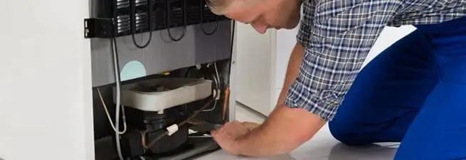 Refrigerator repair technician servicing the compressor and condenser area in Hollywood, FL