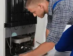Refrigerator repair technician servicing the compressor and condenser area in Hollywood, FL